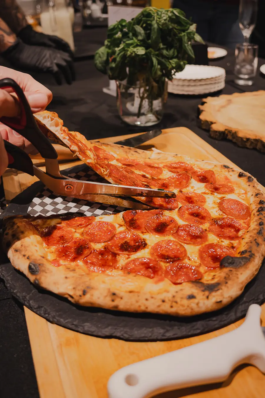 Pizza Pepperoni entera sobre pizarra, cortándose con tijera